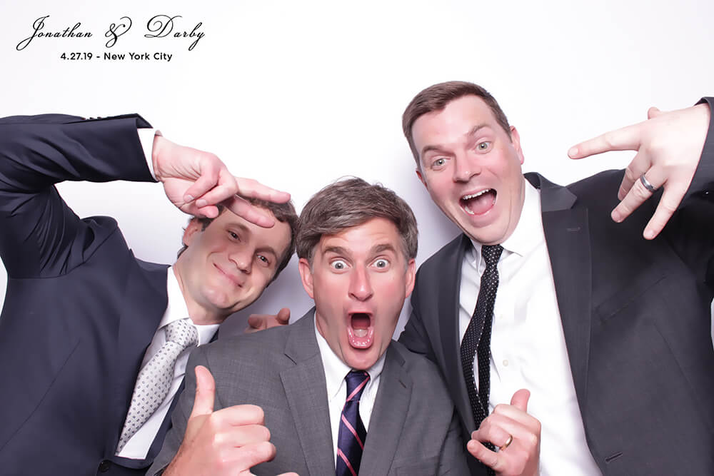 Jonathan & Darby's Wedding Photo Booth three friends pose with funny faces and hand signs in a Photo Booth in front of a bright white backdrop at the wedding of Jonathan and Darby